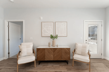 A living room with two chairs and a table and two pictures on the wall